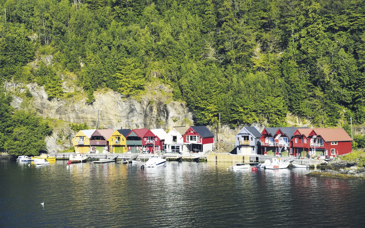 Bunte Holzhäuser und Boote am Hardangerfjord, Norwegen, umgeben von Wald und Bergen.