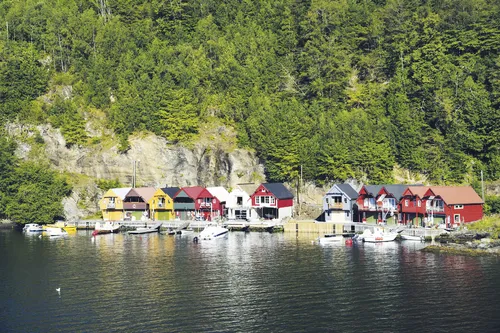 Bunte Holzhäuser und Boote am Hardangerfjord, Norwegen, umgeben von Wald und Bergen.