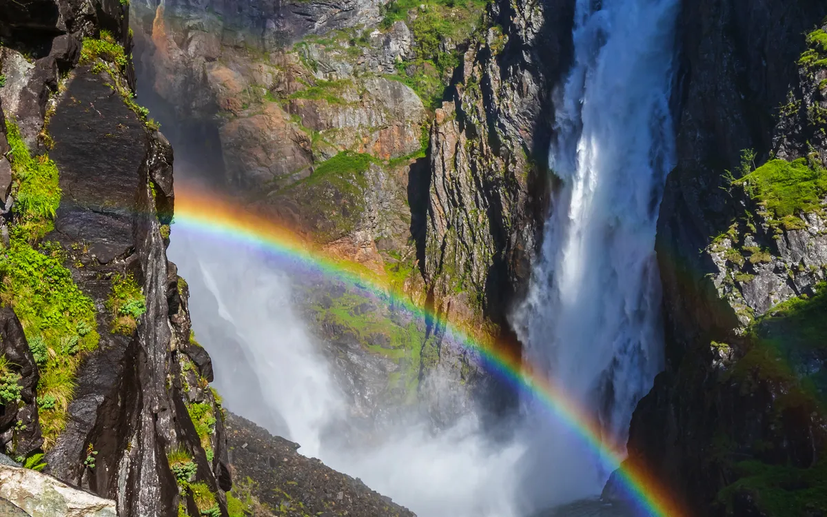 Wasserfall Vøringsfossen in Norwegen mit einem Regenbogen im Vordergrund.