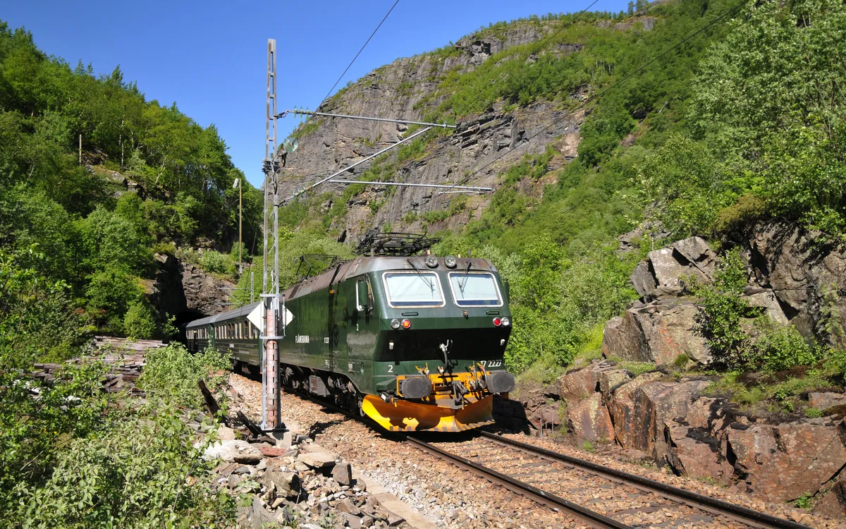 Flåmsbana fährt durch malerische norwegische Landschaft mit Felsen und grüner Vegetation.