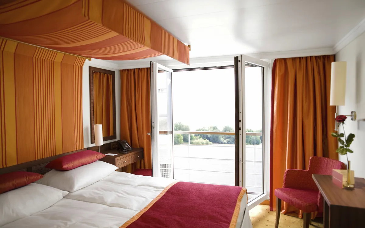 Kabine mit Doppelbett, Sitzgelegenheit und Balkon auf einem Schiff.