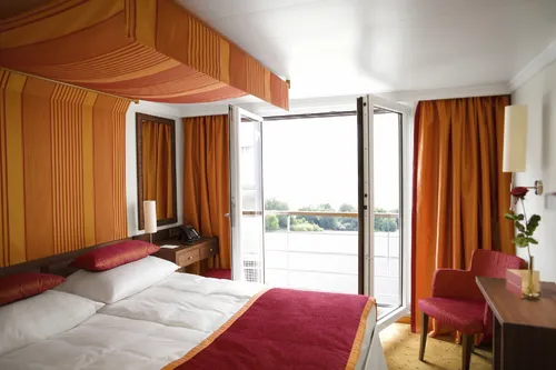 Kabine mit Doppelbett, Sitzgelegenheit und Balkon auf einem Schiff.
