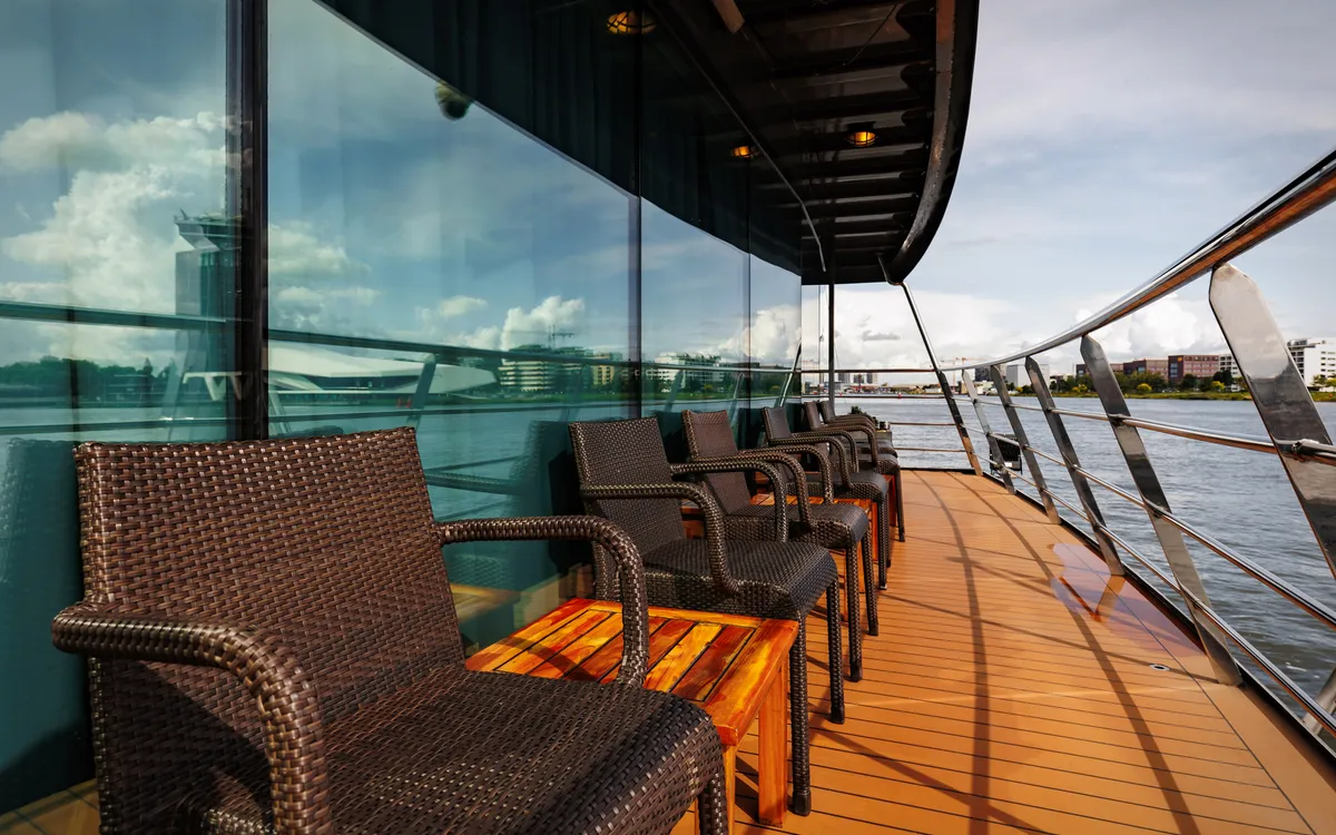 Rattansessel auf sonnigem Deck mit Aussicht auf das Wasser.