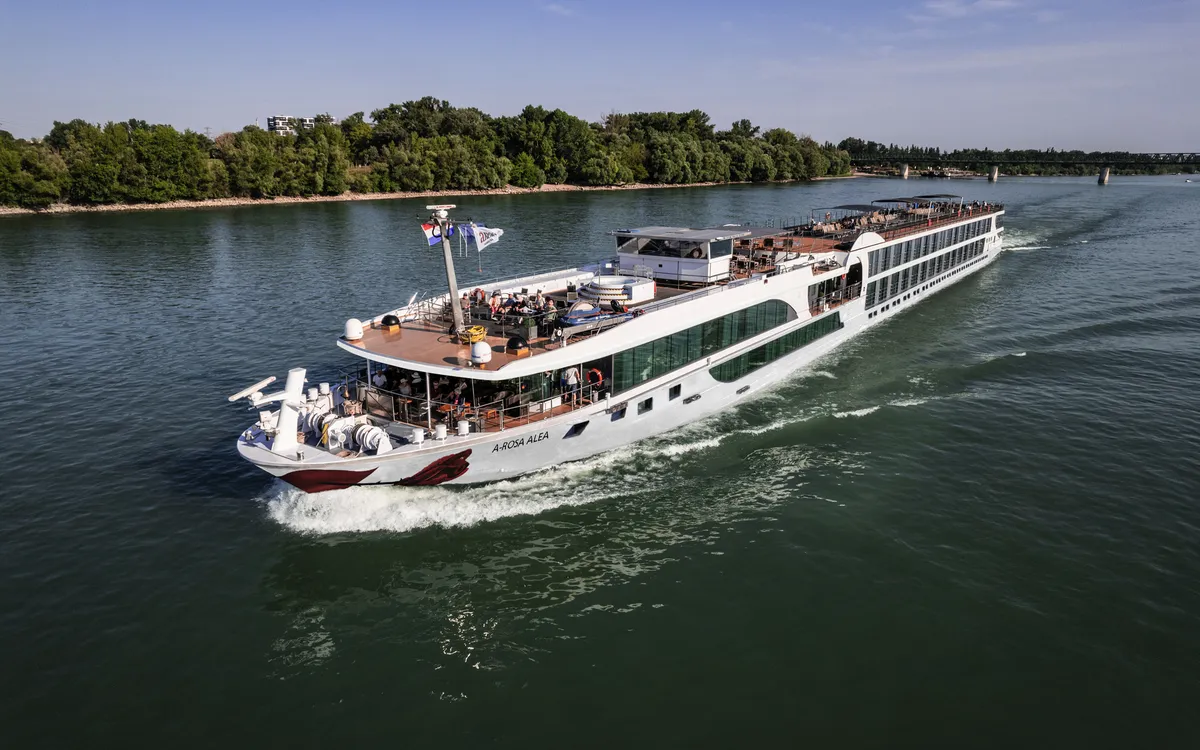 Passagierschiff fährt auf einem Fluss an bewaldetem Ufer entlang.