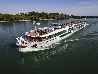 Passagierschiff fährt auf einem Fluss an bewaldetem Ufer entlang.