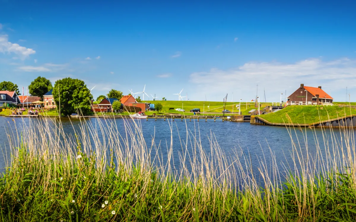 Panorama von Harlingen, Friesland mit Wasser, Leuchtturm und Windrädern bei blauem Himmel.