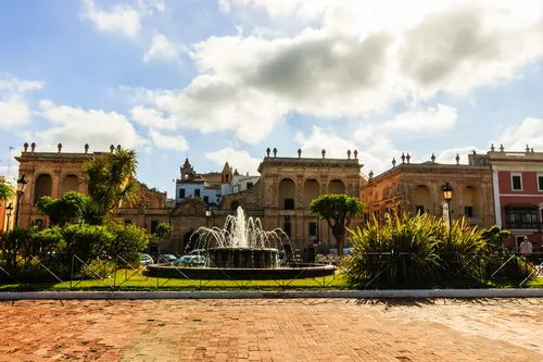 Historische Gebäude und Brunnen in Ciutadella, Menorca, unter bewölktem Himmel.