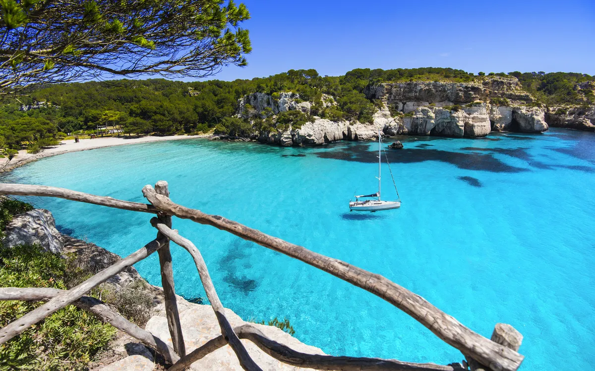 Türkisfarbenes Wasser am Strand Cala Macarella auf Menorca, umrahmt von Felsen und Wald.