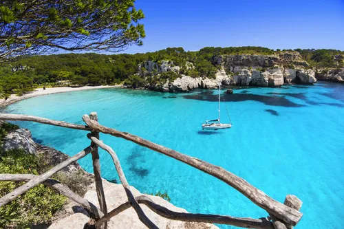 Türkisfarbenes Wasser am Strand Cala Macarella auf Menorca, umrahmt von Felsen und Wald.