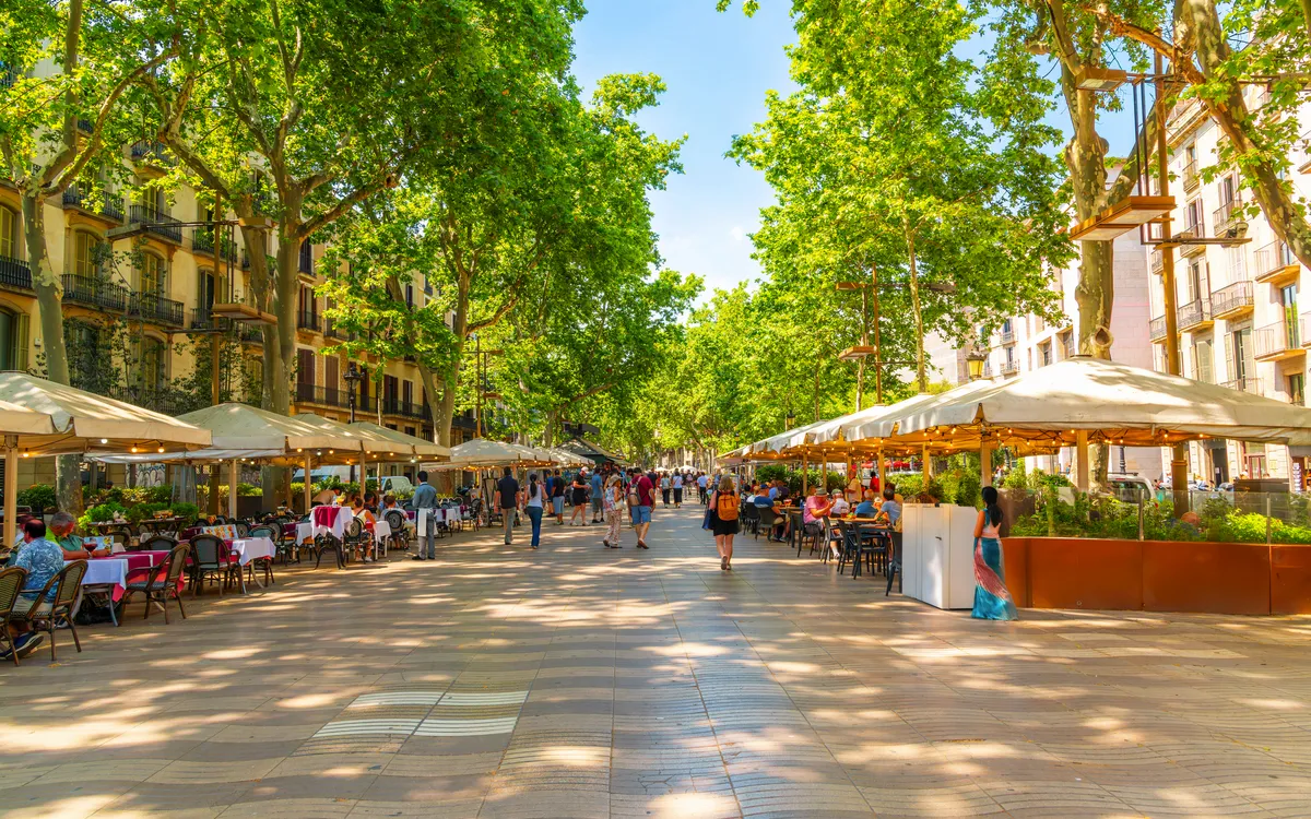 Menschen flanieren auf der von Bäumen gesäumten La Rambla in Barcelona.