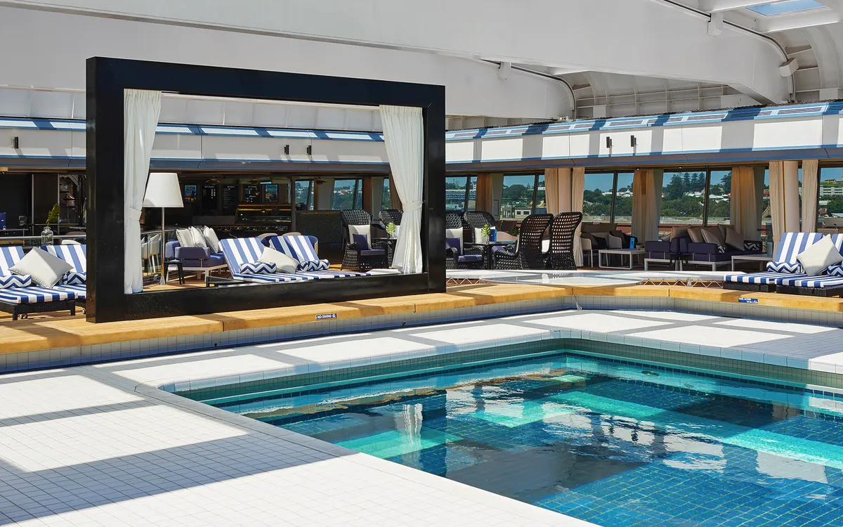 Poolbereich mit weißen und blauen Liegestühlen und einem großen dekorativen Rahmen.