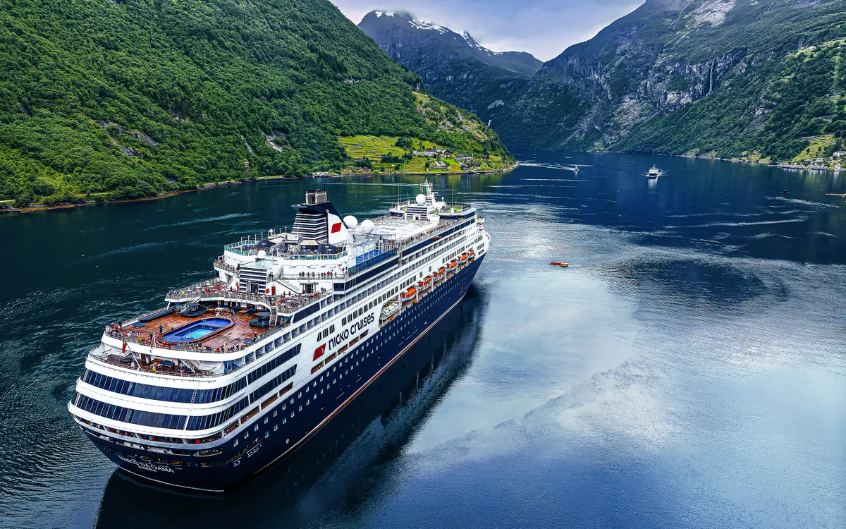 Kreuzfahrtschiff im Geirangerfjord, umgeben von Bergen und Wasser.