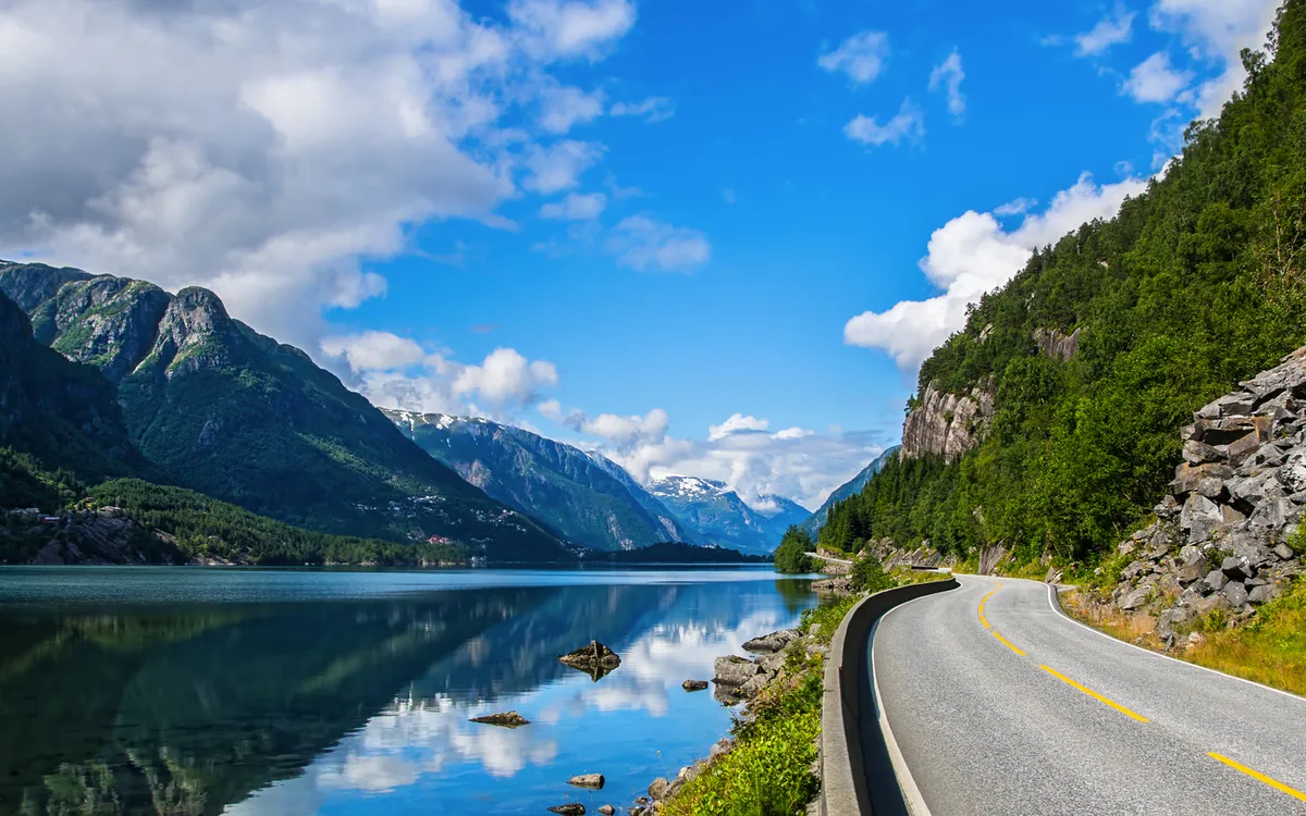 Straße entlang eines Fjords in Norwegen mit Bergen und blauen Himmel.