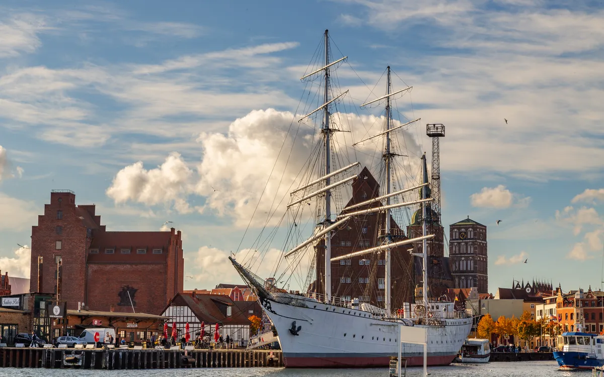 Hafen von Stralsund mit Segelschiff Gorch Fock, Segelboote und historische Gebäude im Hintergrund.