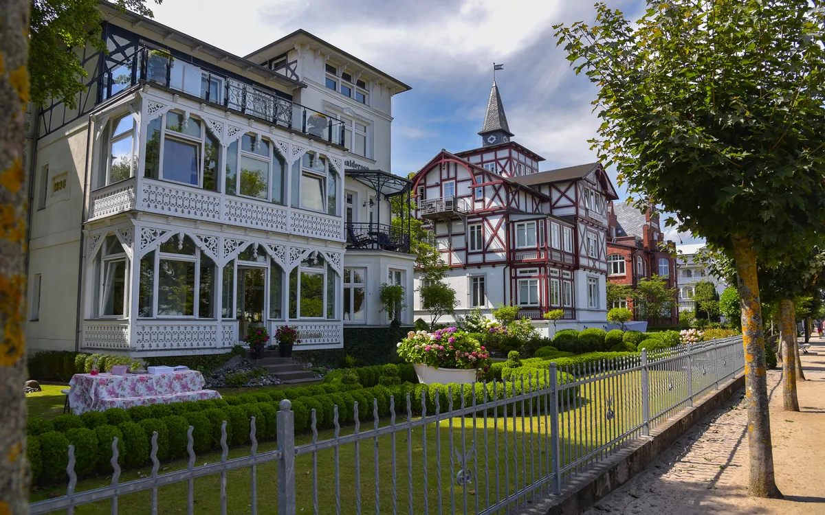 Historische weiße und rote Villen an einer von Bäumen gesäumten Straße.