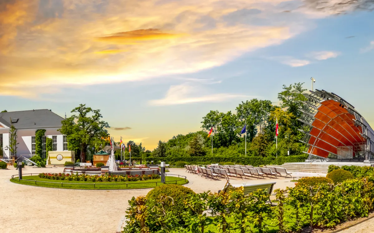 Parkanlage mit Gebäude, modernen Skulpturen und Fahnen im Sonnenuntergang.