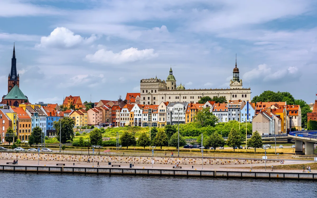 Stadtansicht mit historischen Gebäuden und Fluss im Vordergrund.
