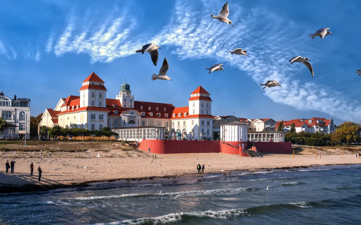 Gebäude mit roten Dächern am Strand mit fliegenden Möwen im Vordergrund