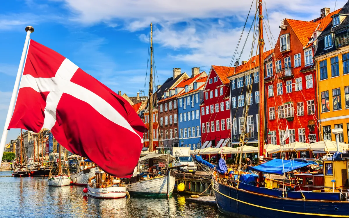 Dänische Flagge weht in Kopenhagens Hafen mit bunten Häusern im Hintergrund.