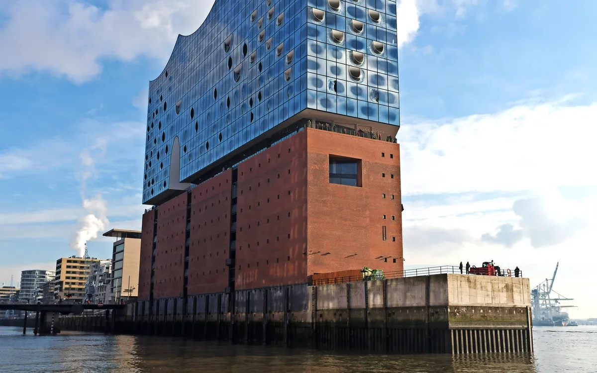 Elbphilharmonie in Hamburg vor blauem Himmel und Wasser im Vordergrund.