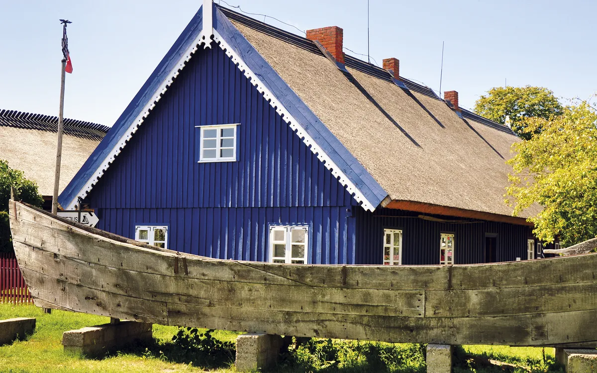 Blaues Holzhaus mit Holzboot, Fenstern und Fensterläden auf grüner Wiese.