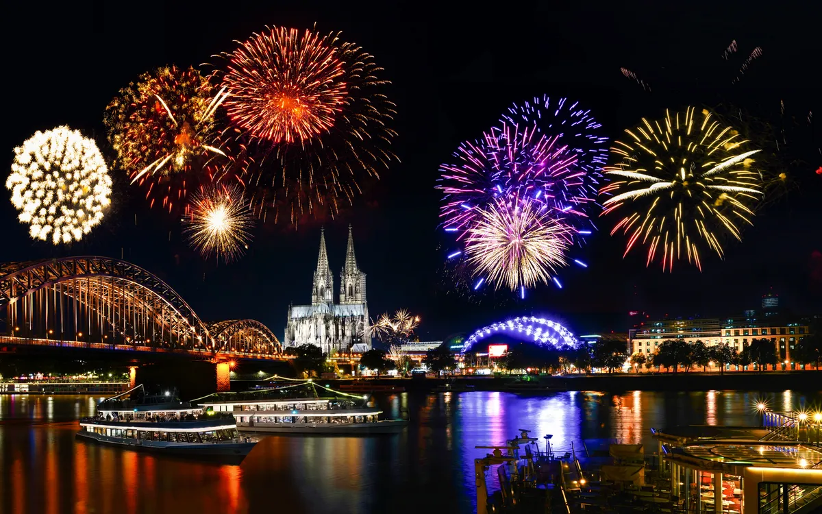 Feuerwerk über Kölner Dom und Rhein bei Nacht, mit beleuchteter Hohenzollernbrücke.