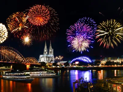 Feuerwerk über Kölner Dom und Rhein bei Nacht, mit beleuchteter Hohenzollernbrücke.