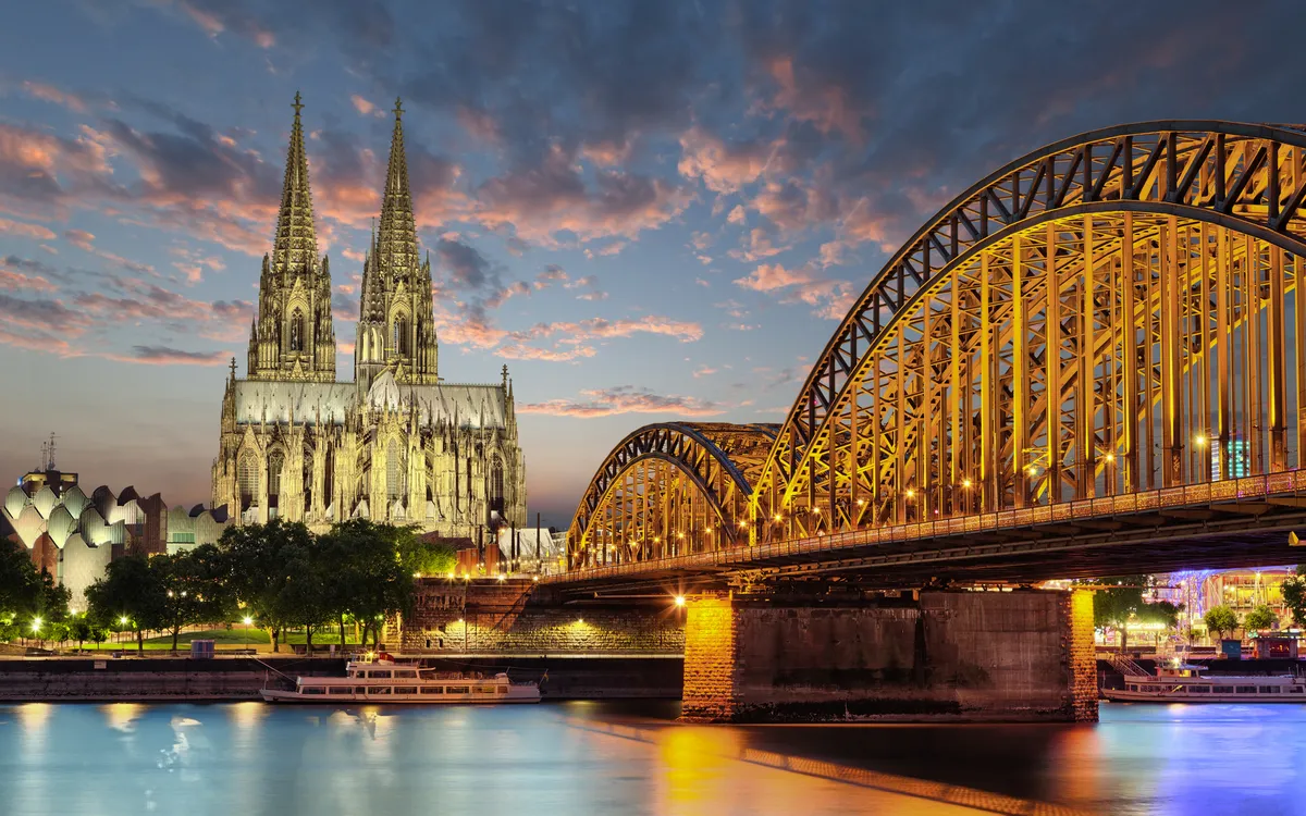 Kölner Dom am Rhein bei Abenddämmerung mit beleuchteter Brücke