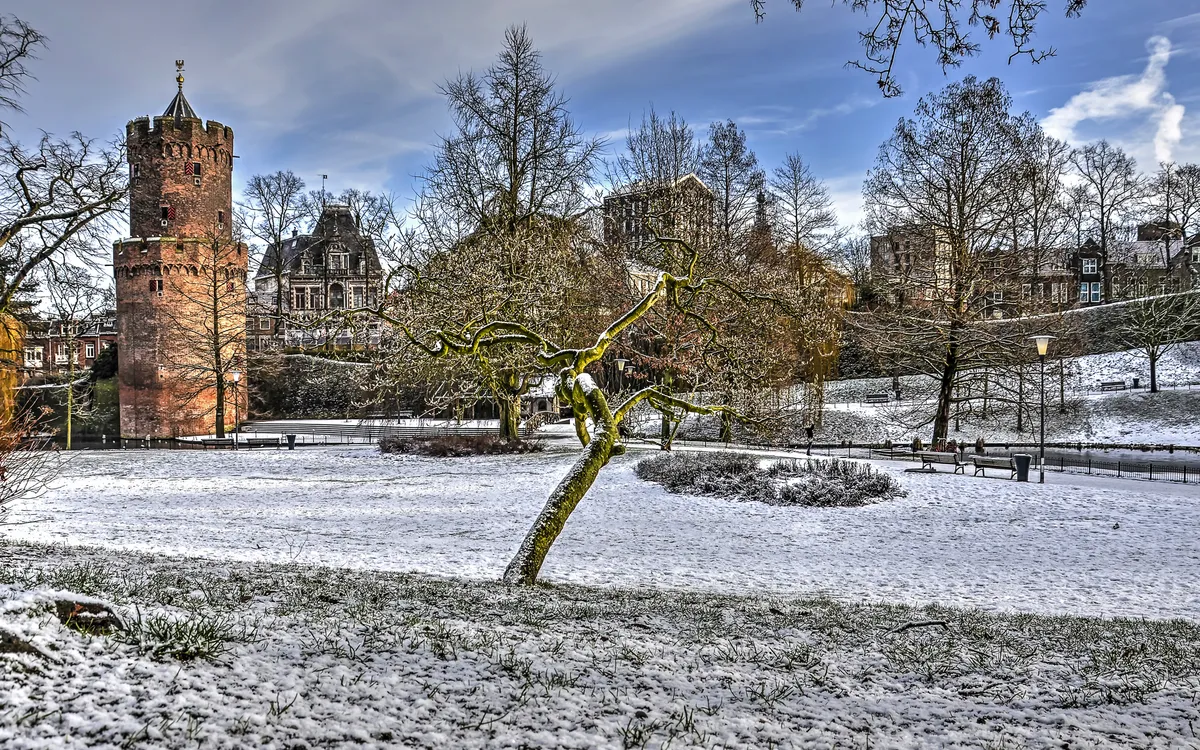 Winterlicher Kronenburg Park in Nijmegen mit Schnee und historischem Turm.