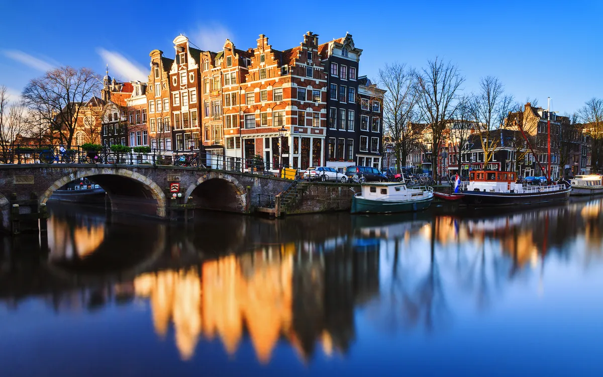 Amsterdamer Grachten im Winter bei klarem Himmel und reflektierendem Wasser.
