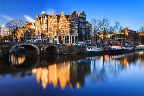 Amsterdamer Grachten im Winter bei klarem Himmel und reflektierendem Wasser.