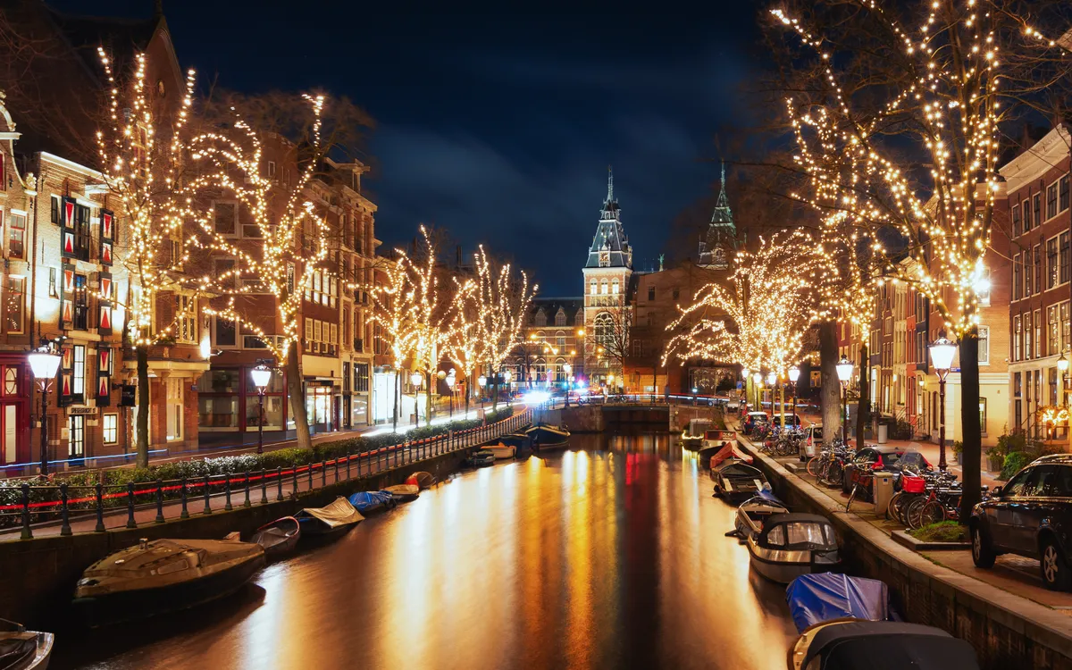 Amsterdam im Winter mit beleuchteten Bäumen am Kanal und Rijksmuseum im Hintergrund.