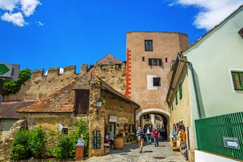 Eine malerische Altstadtgasse mit historischem Tor und Spaziergängern.
