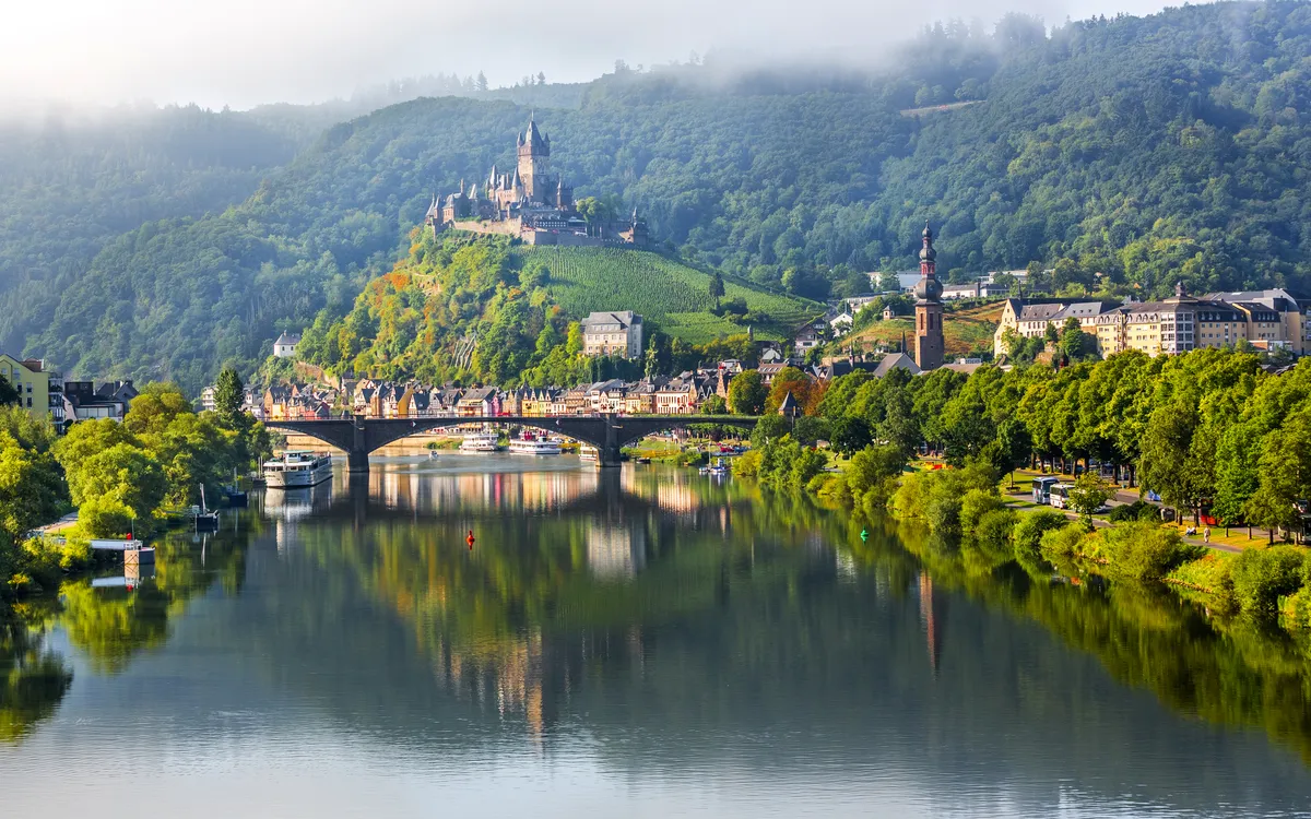 Burg und Stadt an einem Fluss, umgeben von grüner Landschaft.