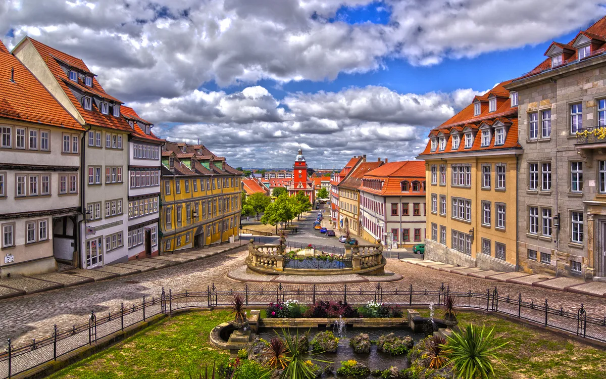 Panoramablick auf einen historischen Platz mit alten Gebäuden und Brunnen.