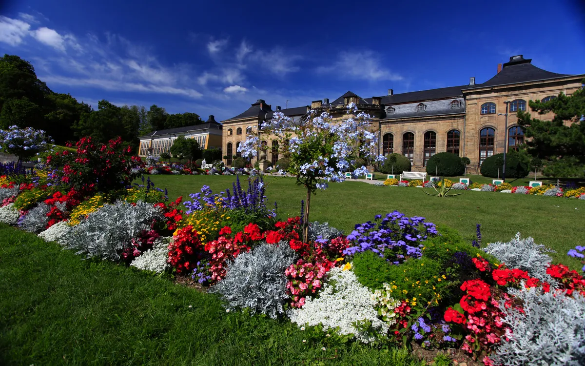 Blumenbeet vor historischem Gebäude im Park bei blauem Himmel.