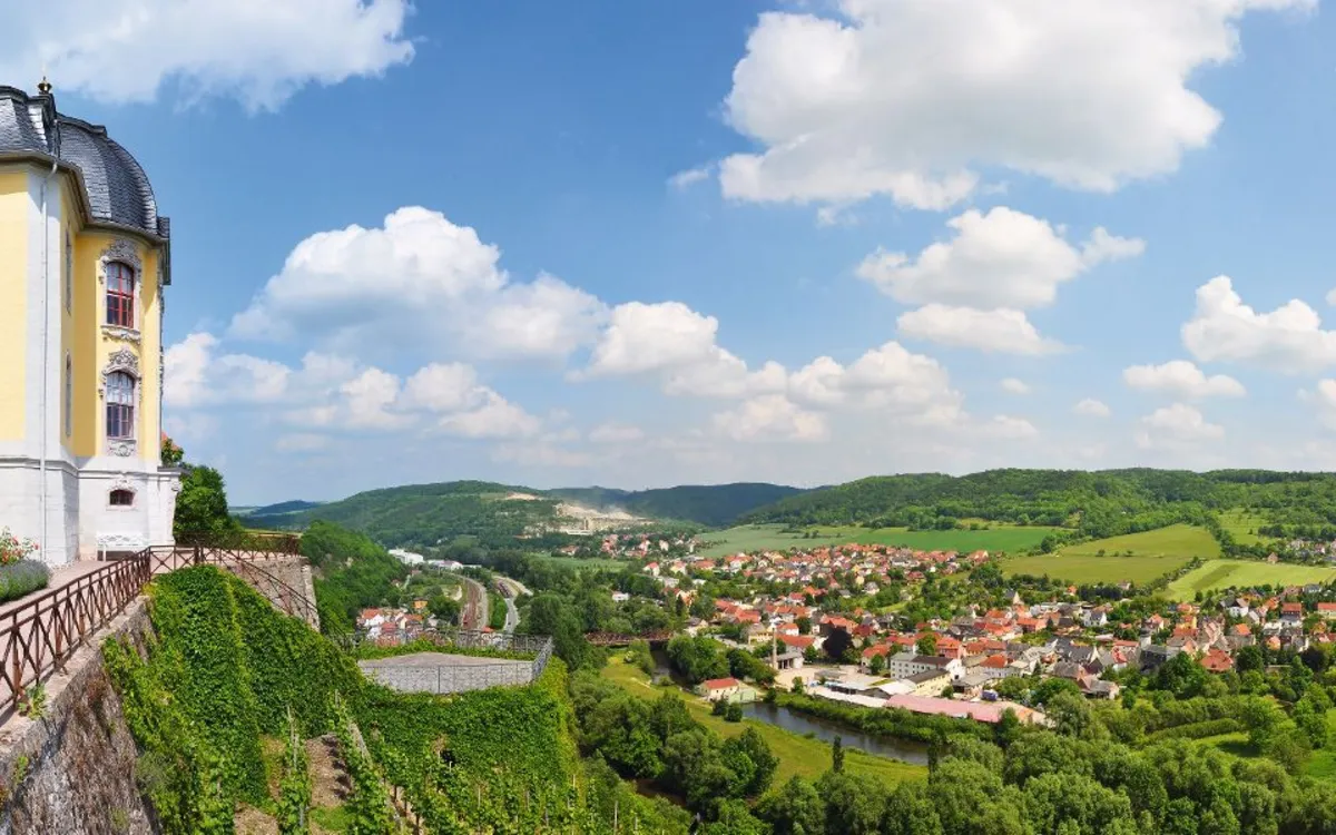 Schloss auf Hügel mit Blick auf grünes Tal und Dorf im Hintergrund.