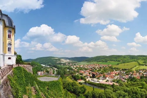 Schloss auf Hügel mit Blick auf grünes Tal und Dorf im Hintergrund.