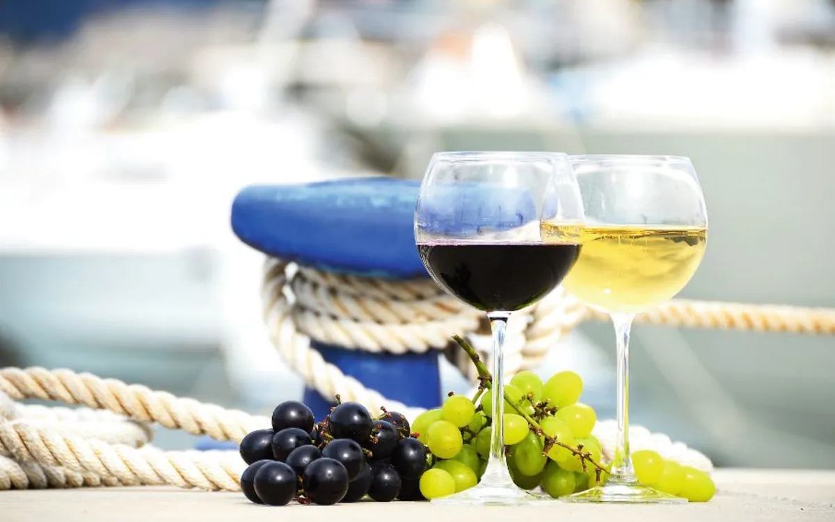 Zwei Gläser Wein und Trauben auf einem Hafengeländer.