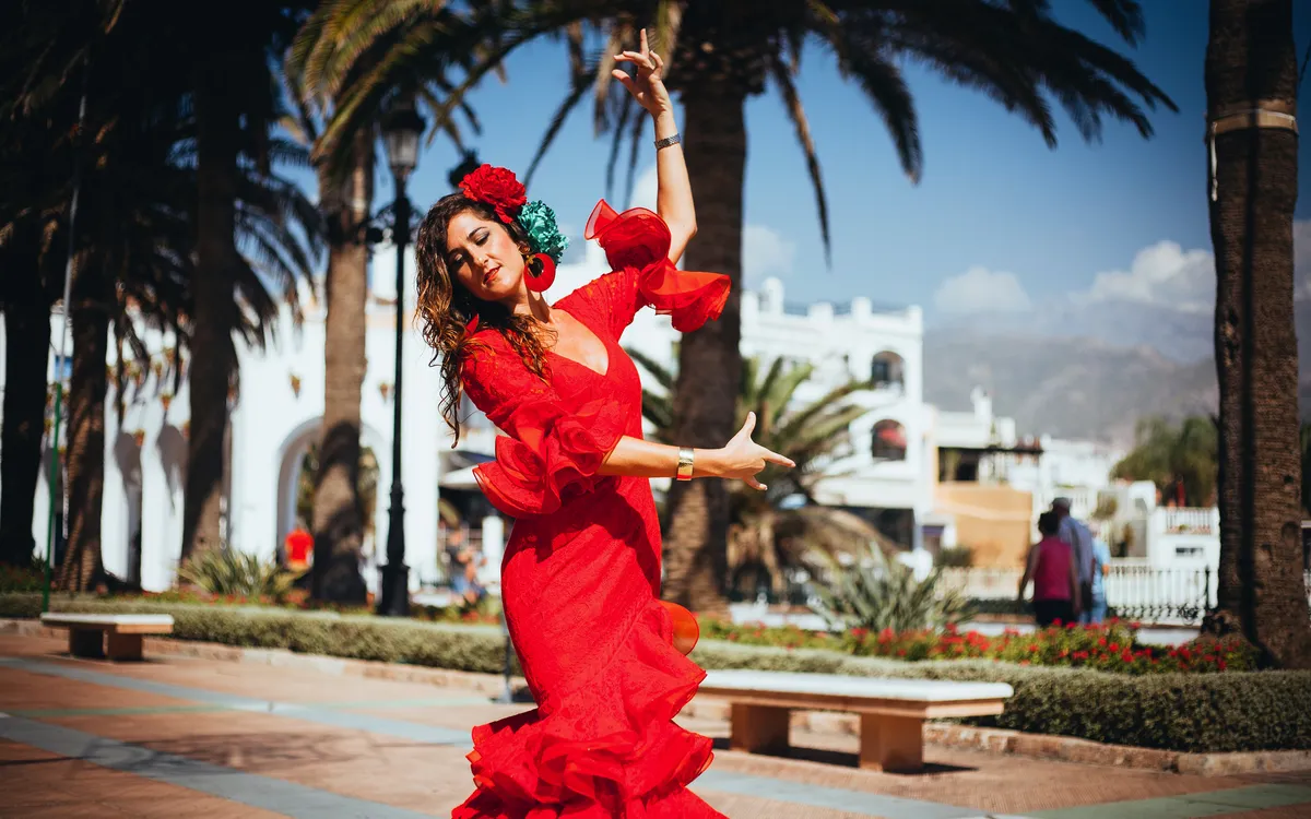 Frau in einem roten Flamenco-Kleid tanzt leidenschaftlich im Freien unter Palmen.