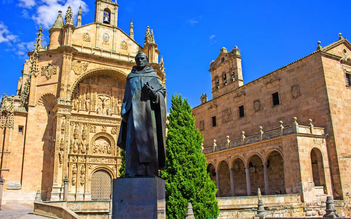 Statue vor historischer Kirche mit reicher Fassade und blauem Himmel.