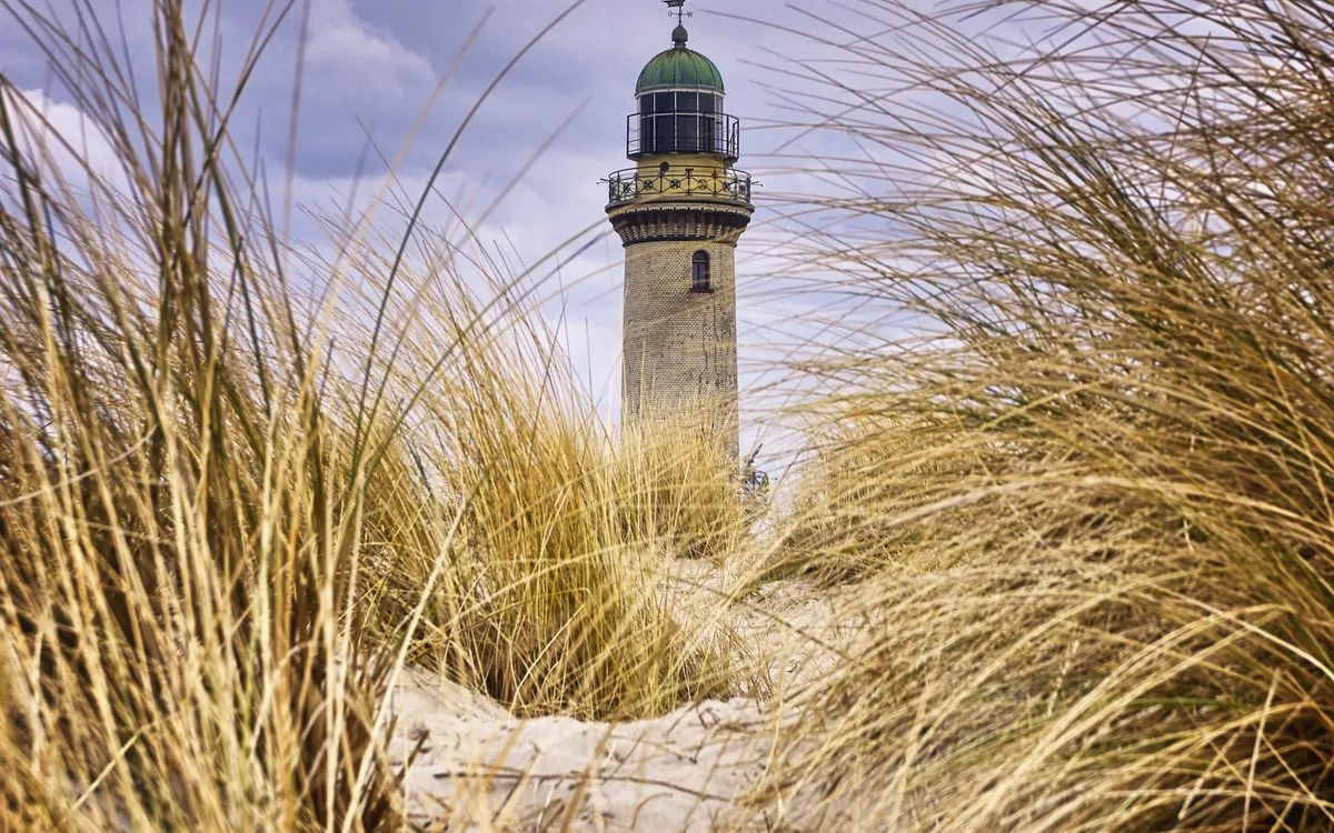 Leuchtturm Warnemünde hinter Dünengras am Strand.