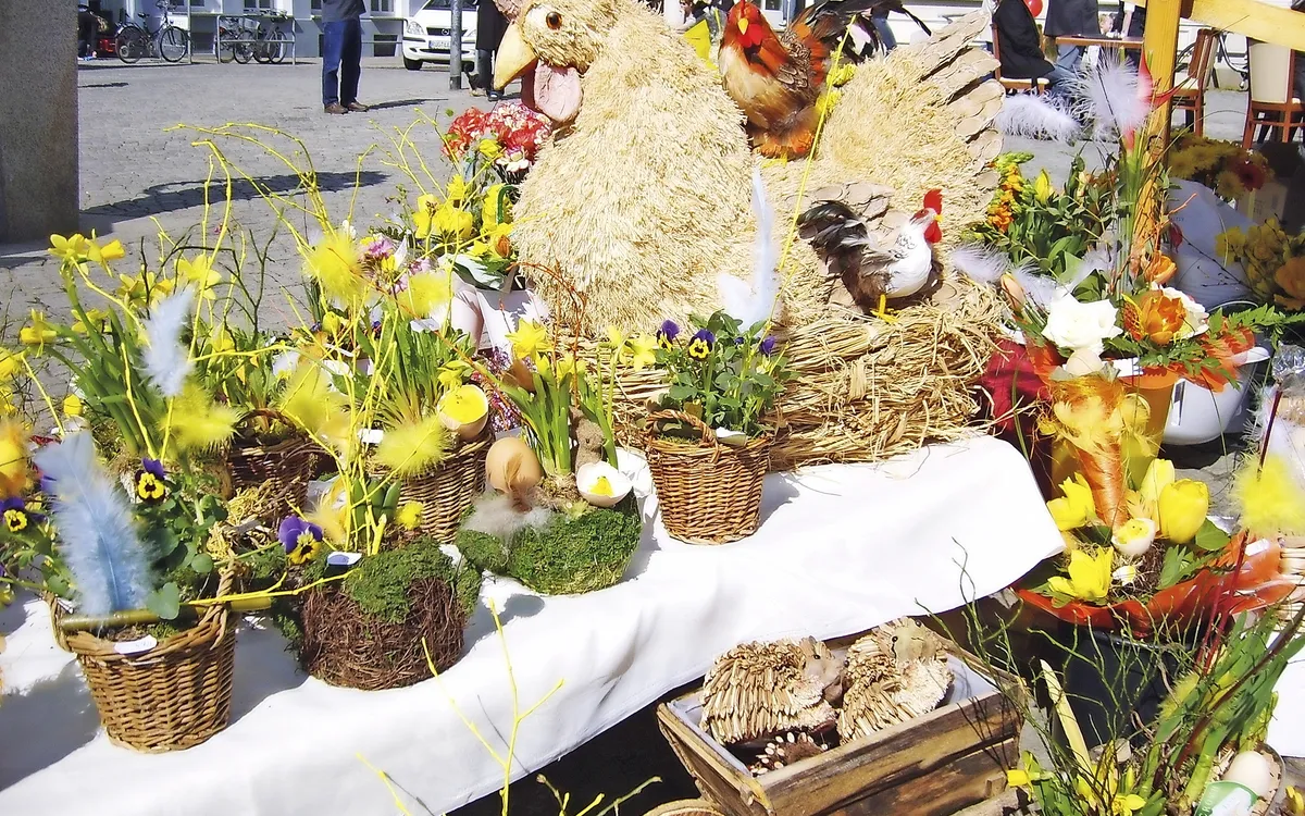 Dekorativer Stand mit bunten Frühlingsblumen und Strohhuhn auf dem Greifswalder Markt.